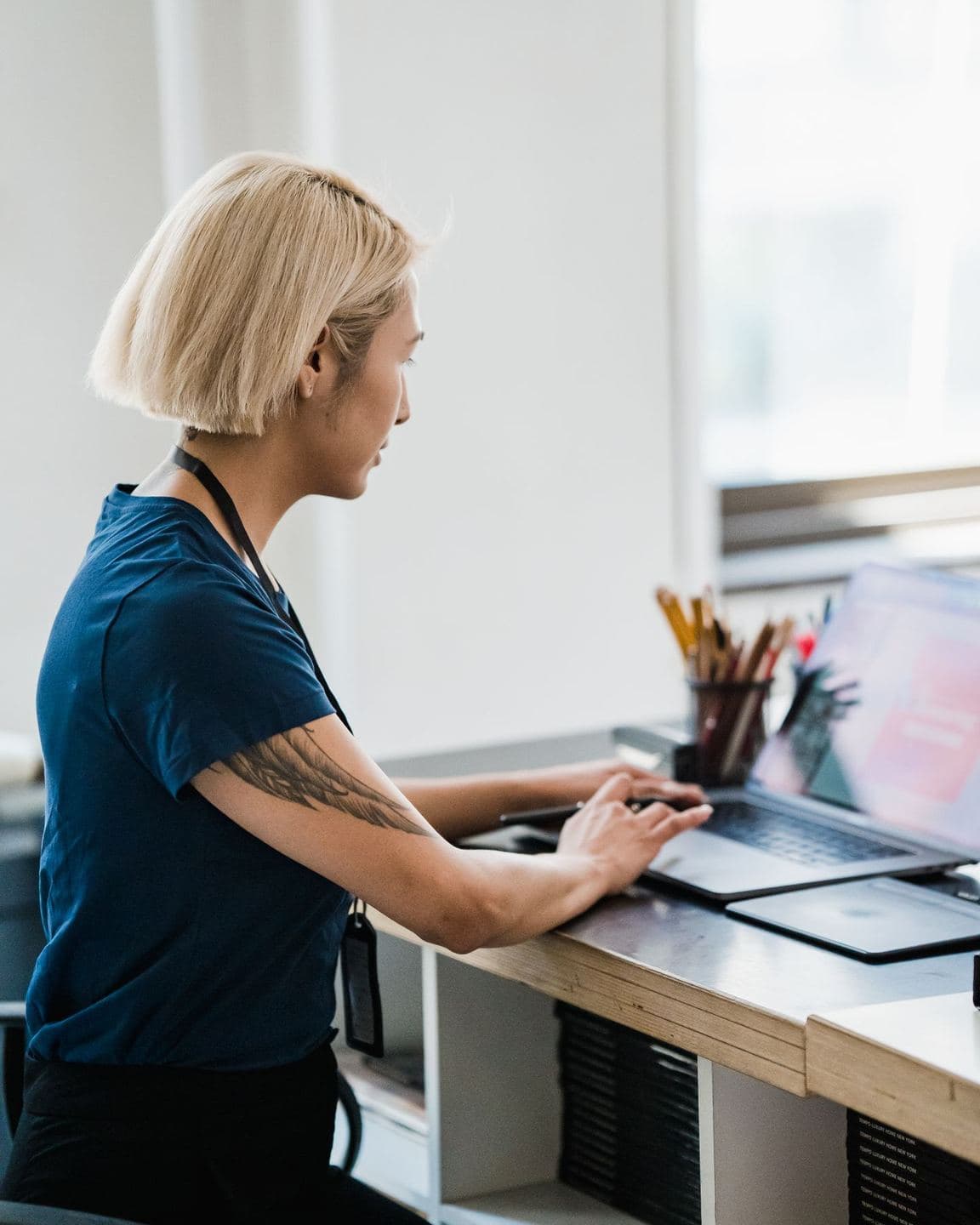 Personne assise de profil à son bureau devant un ordinateur portable, trois zones de douleur repérées : nuque, dos et poignet
